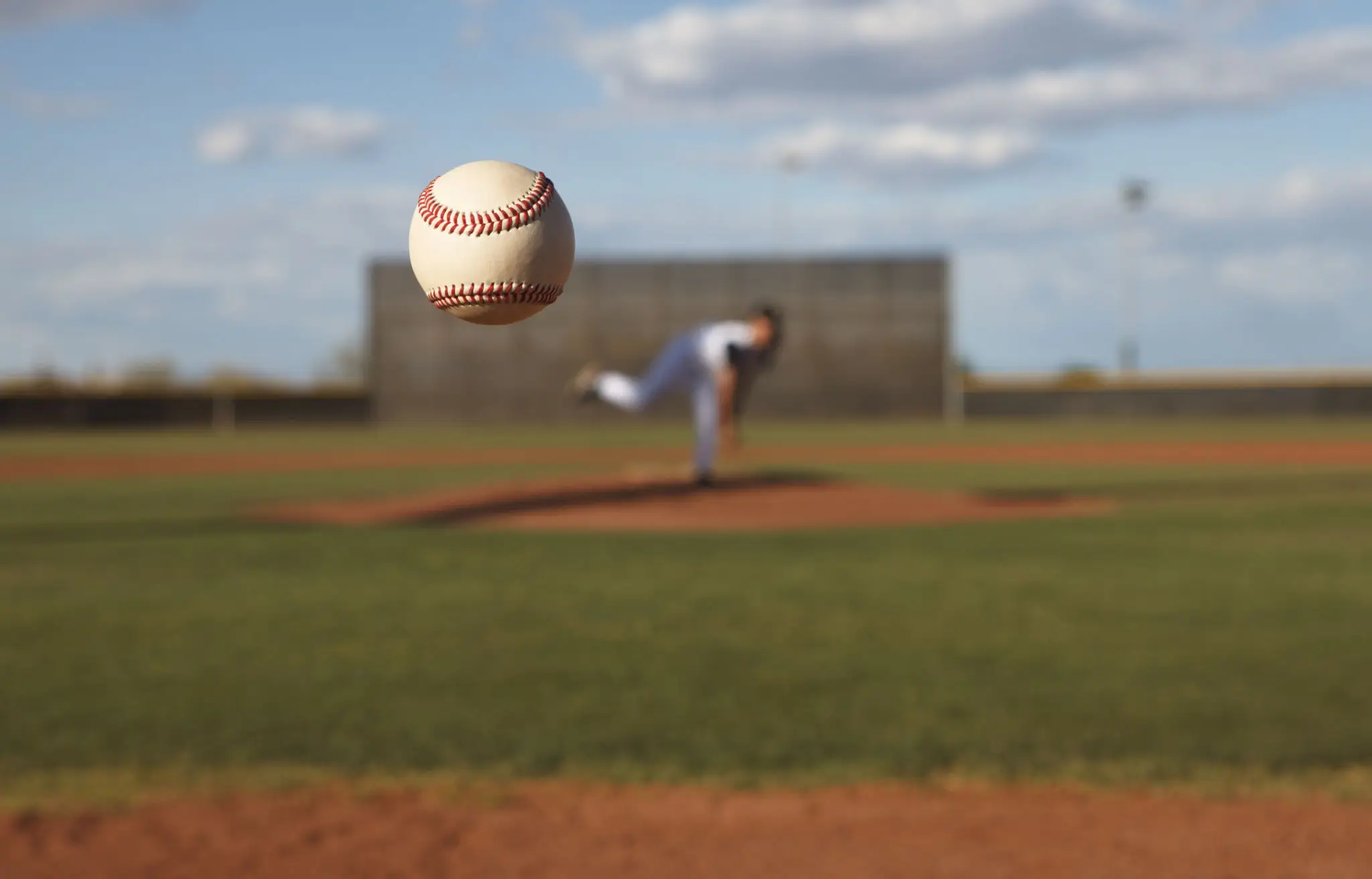 Baseball flying toward the camera with pitcher in background.