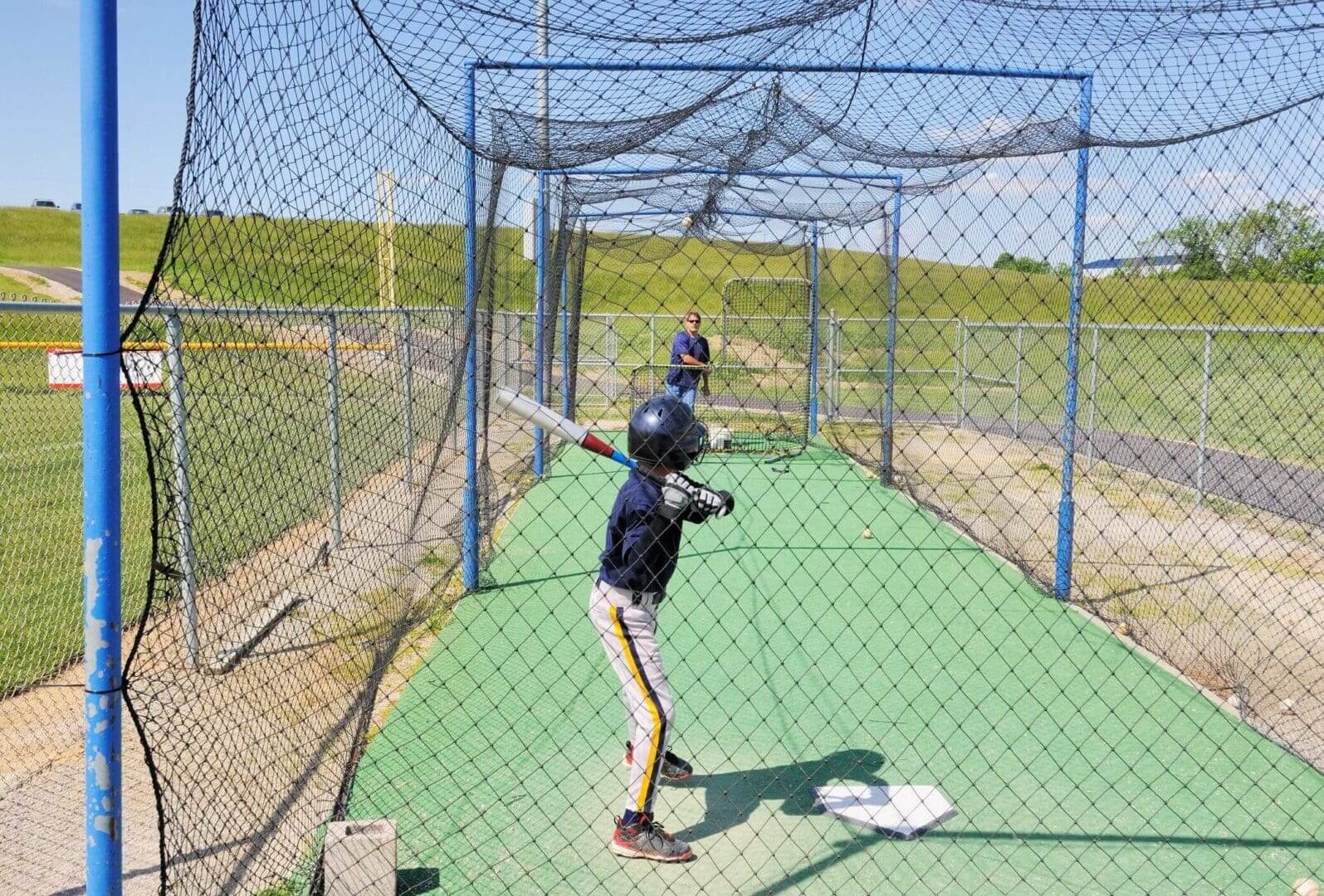 Child practicing batting in a baseball cage.