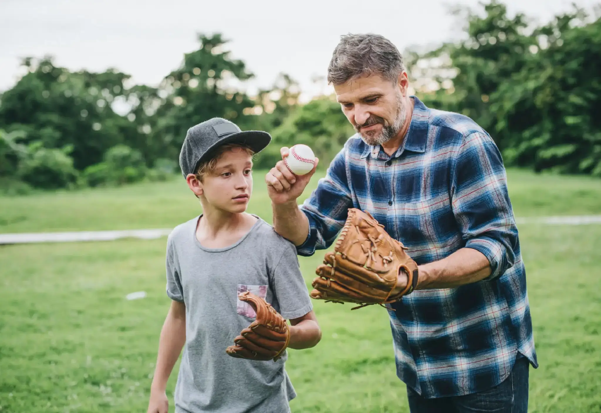 Man teaching boy to play baseball outdoors.