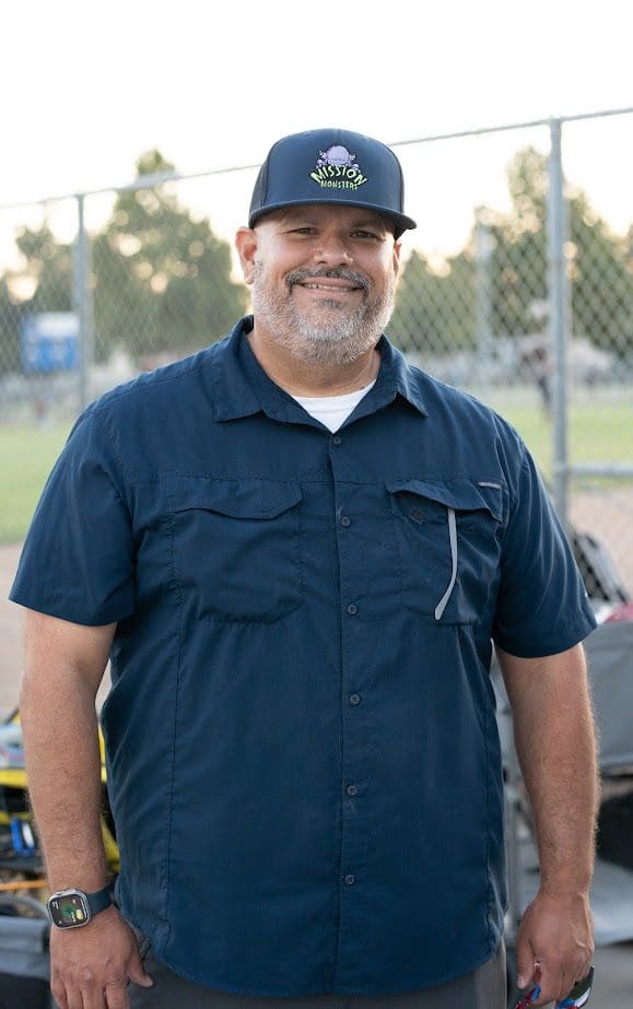 Smiling man in navy blue shirt and baseball cap outdoors.
