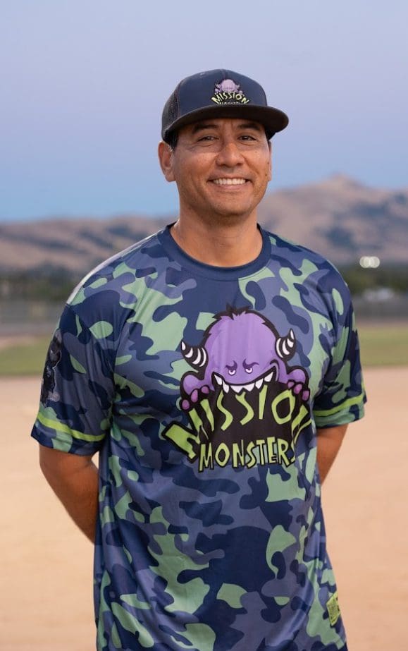 Man smiling in a camo shirt with a purple cartoon character and text.