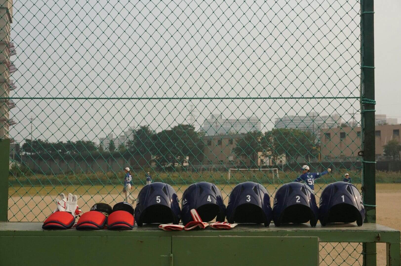Baseball helmets and gloves lined up on a bench at the field.