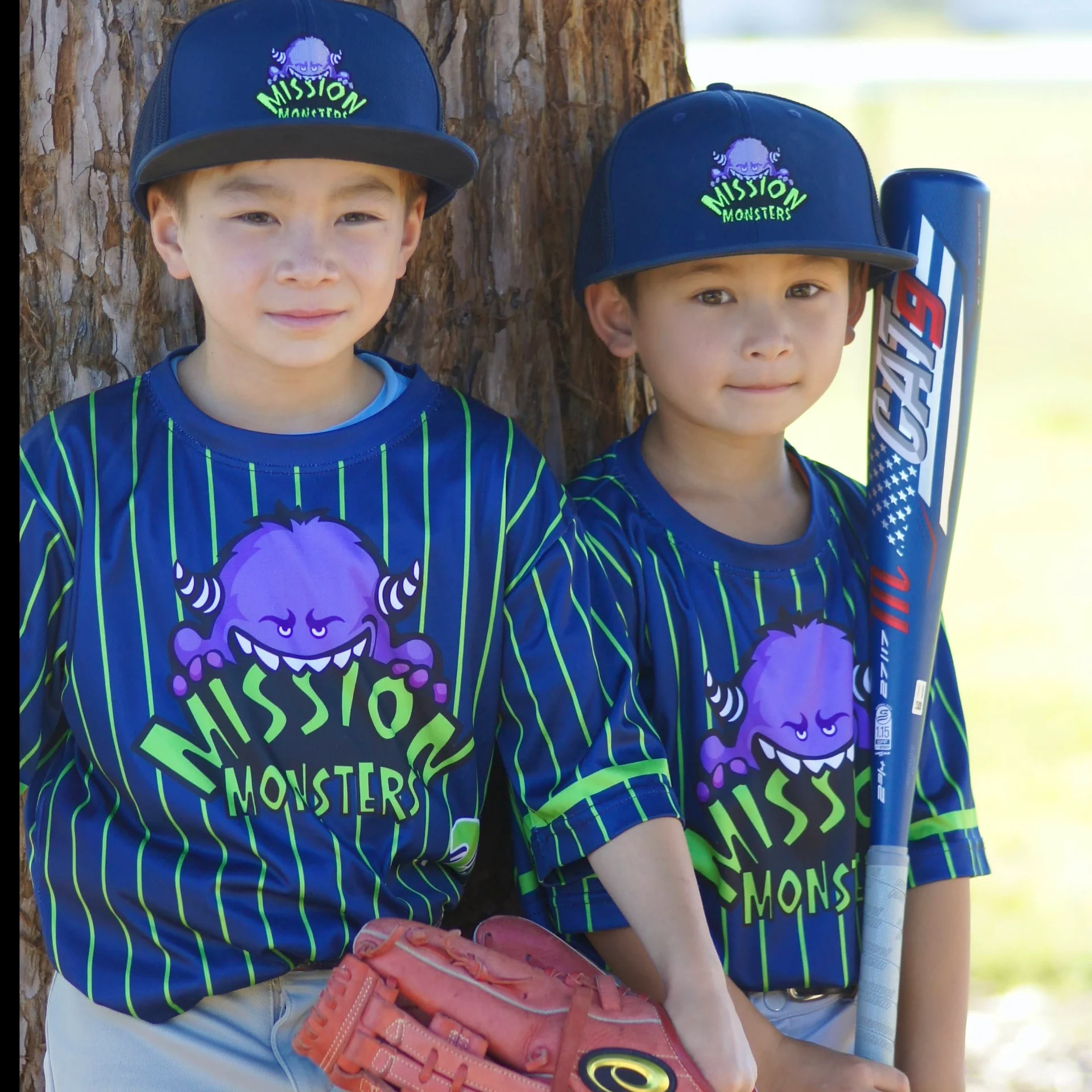 Two young girls in baseball uniforms holding a bat and glove.